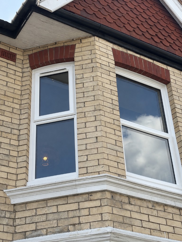 White bay window on a buff brick house under a red-tiled roof